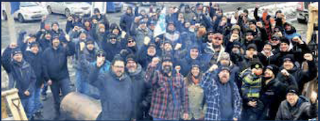 Un groupe de quelque 50 personnes portant des manteaux fonc&eacute;s et chapeaux d&rsquo;hiver soul&egrave;vent le poing et sourient &agrave; la cam&eacute;ra &ndash; solidarit&eacute; sur la ligne de piquetage &agrave; Contrec&oelig;ur, au Qu&eacute;bec.