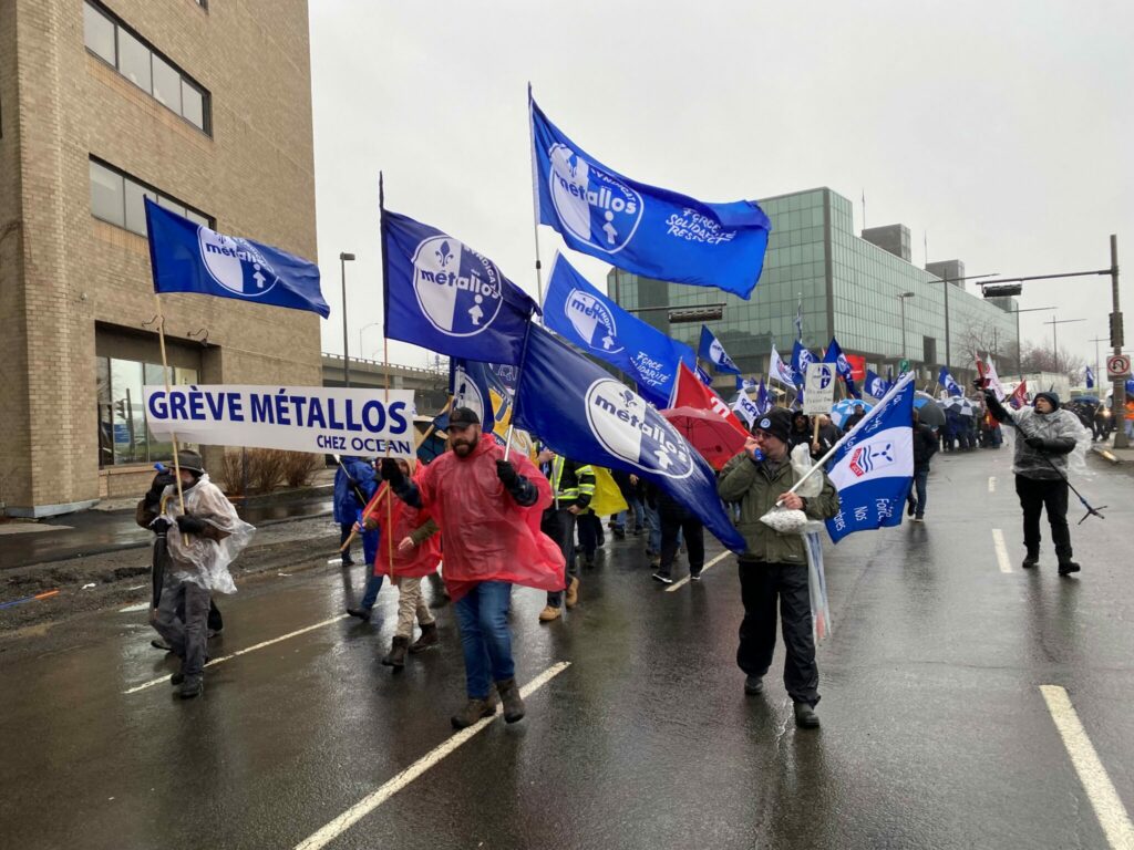 A parade of striking Métallos marching down a street waving