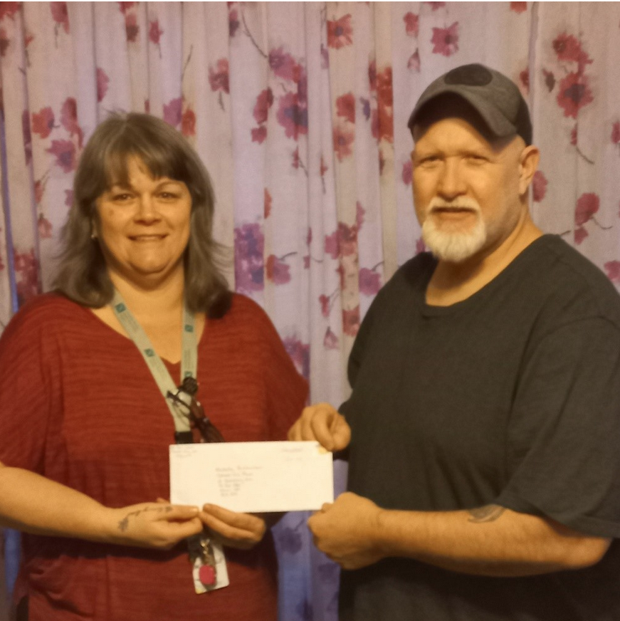 Image: Two people are pictured facing the camera smiling, shown from the waist up, holding a cheque that is being presented by the person on the right to the person on the left.