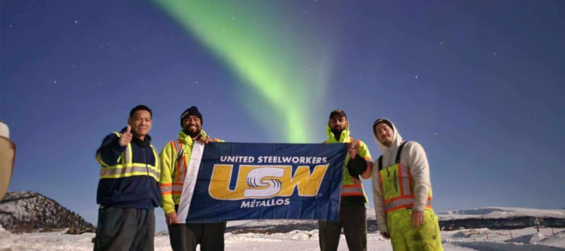 Workings from Parsons Inc holding a USW flag under the Northern Lights