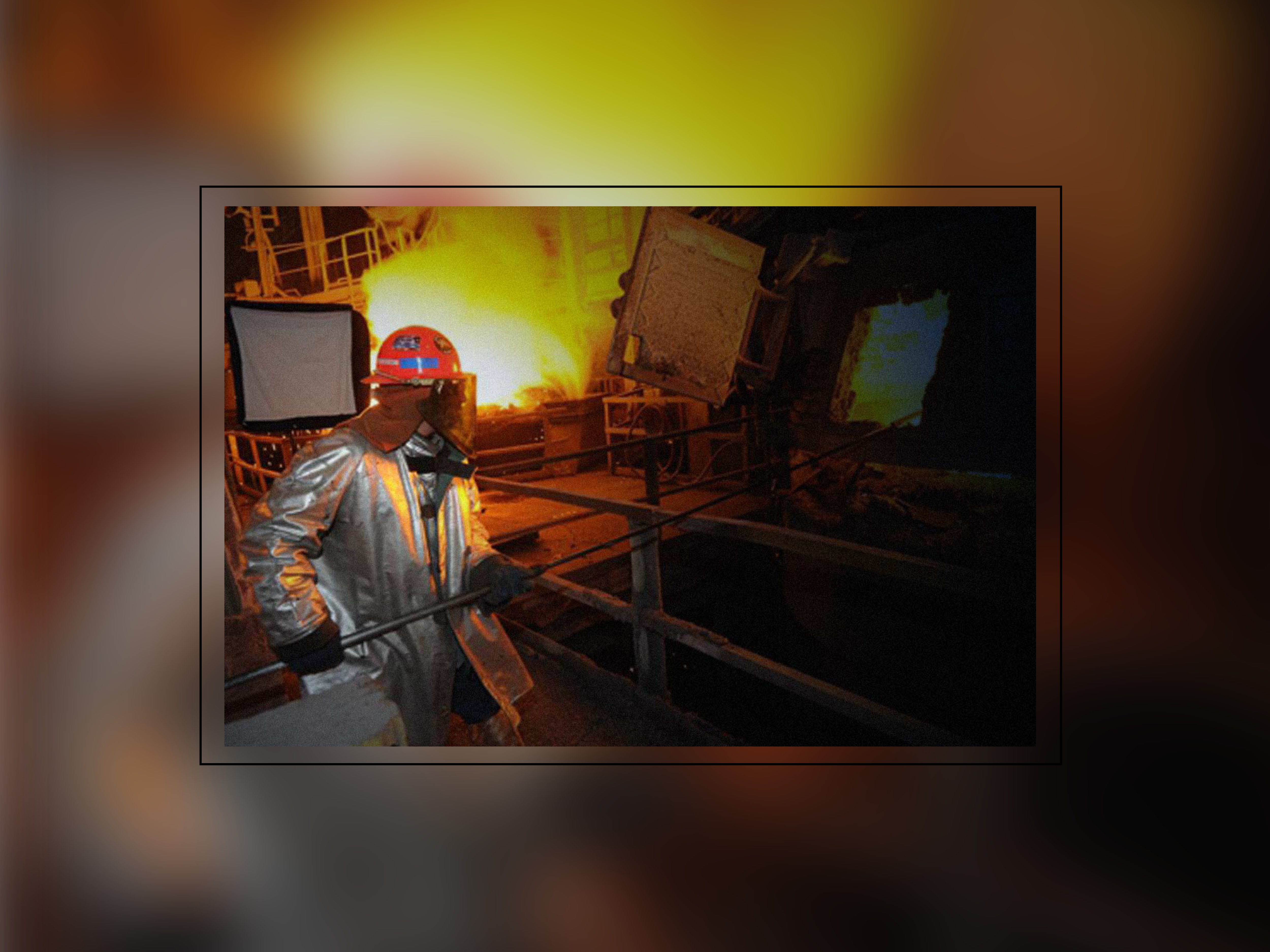 A steel worker in full safety gear working in front of a blast furnace.