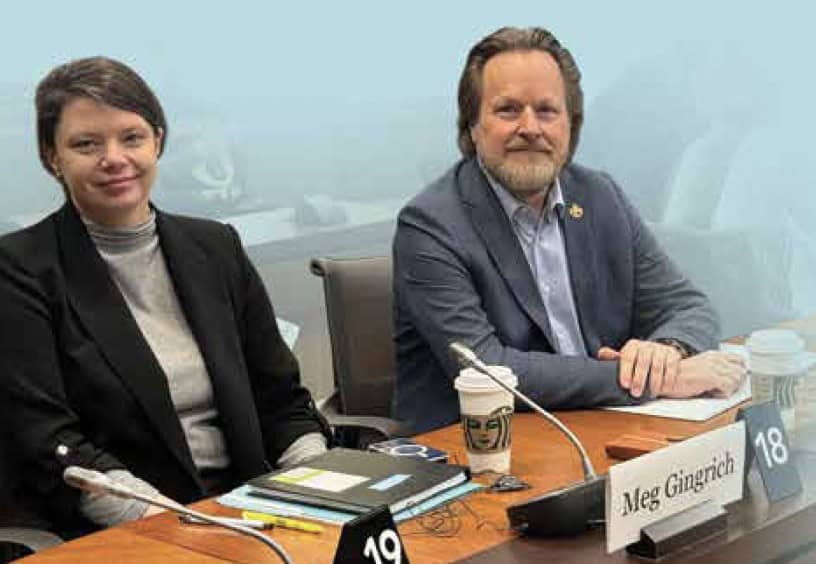 Image : - Deux personnes assises dans une salle de conférence fixent la caméra lors de la prise d’une photo. La personne à droite porte un veston gris et celle à sa gauche un veston noir et un chandail gris.