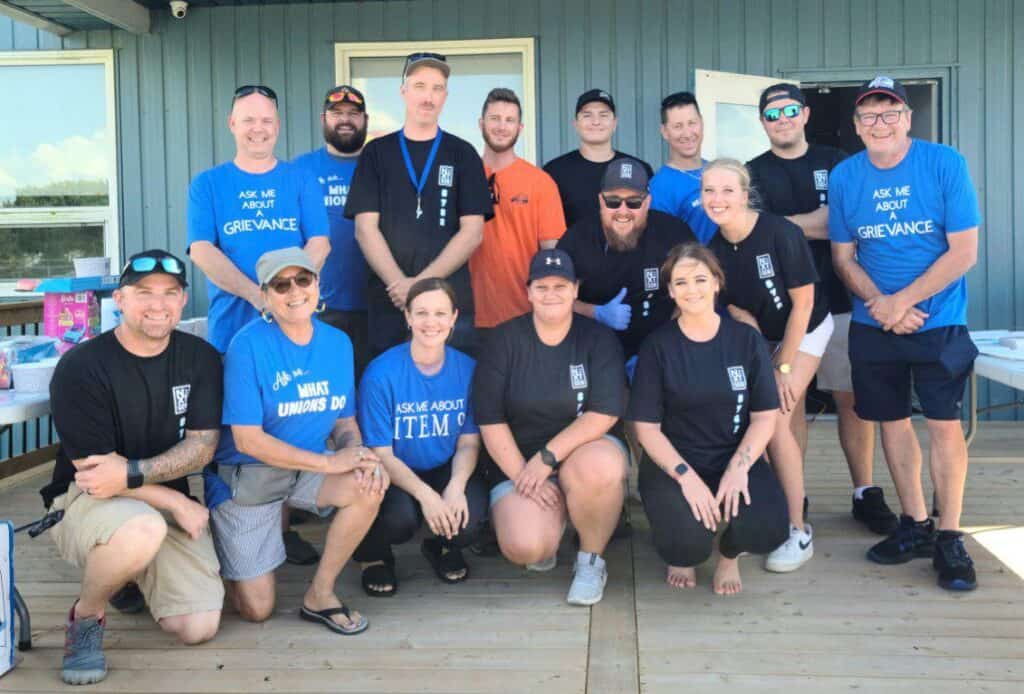 Image : Une photo de 15 personnes, sur deux rangs, face à l’appareil photo, dont certaines portent des T-shirts bleus portant l’inscription « demandez-moi ».