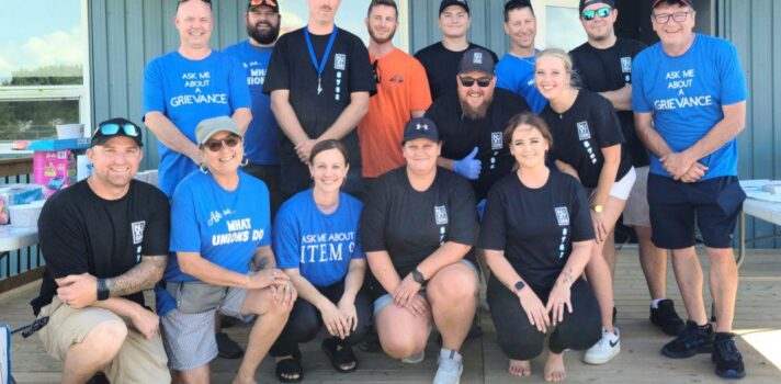 Image : Une photo de 15 personnes, sur deux rangs, face à l’appareil photo, dont certaines portent des T-shirts bleus portant l’inscription « demandez-moi ».