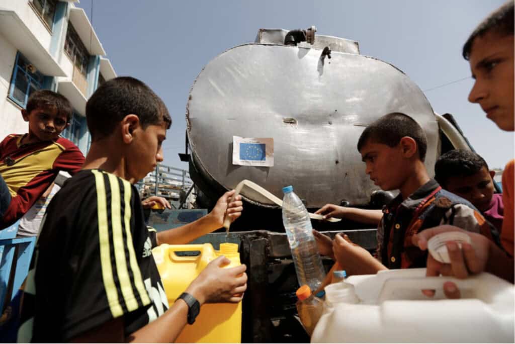 A group of kids holding empty water gallons lining up in front of a water container