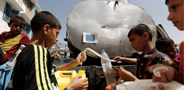 A group of kids holding empty water gallons lining up in front of a water container