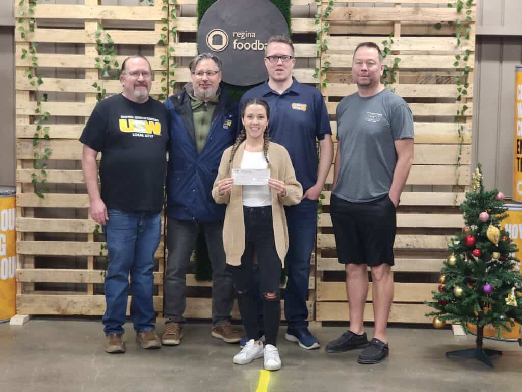 Five USW members taking a photo with a food bank representative. The rep is holding a cheque.