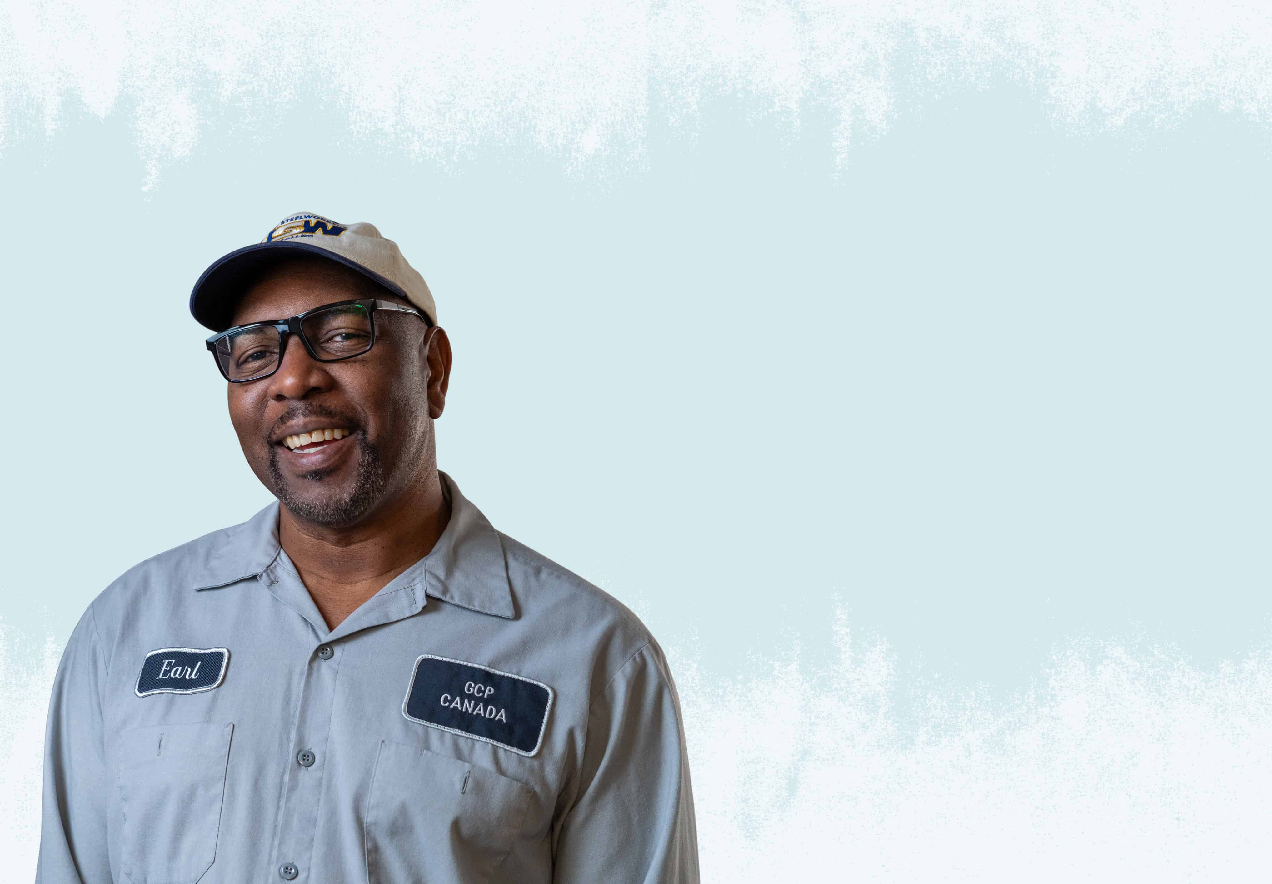 A racialized person wearing a light blue work uniform and grey hat.