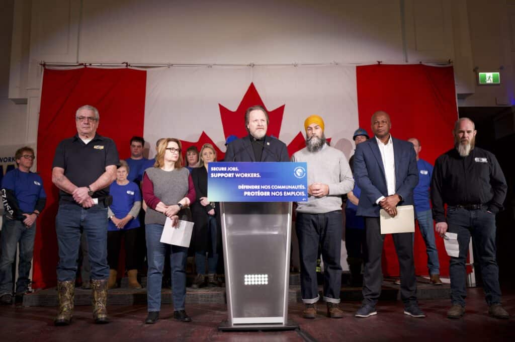 Director of the United Steelworkers union Marty Warren stands behind a podium next to Jagmeet Singh, Leader of the federal NDP, and Kevon Stewart, USW District 6 Director, and among other labour leaders.