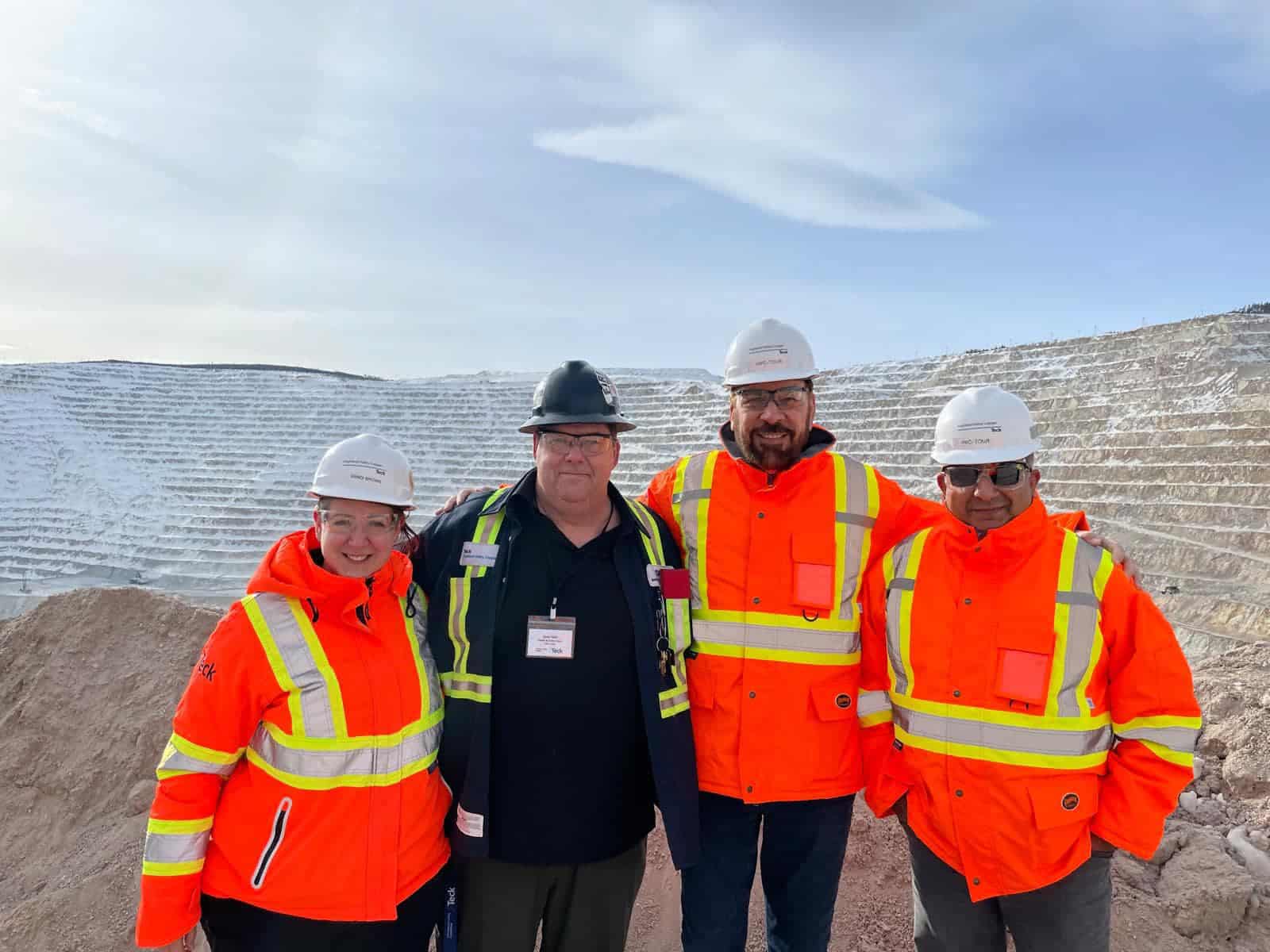 Four people in safety gear and hard hats smiling.