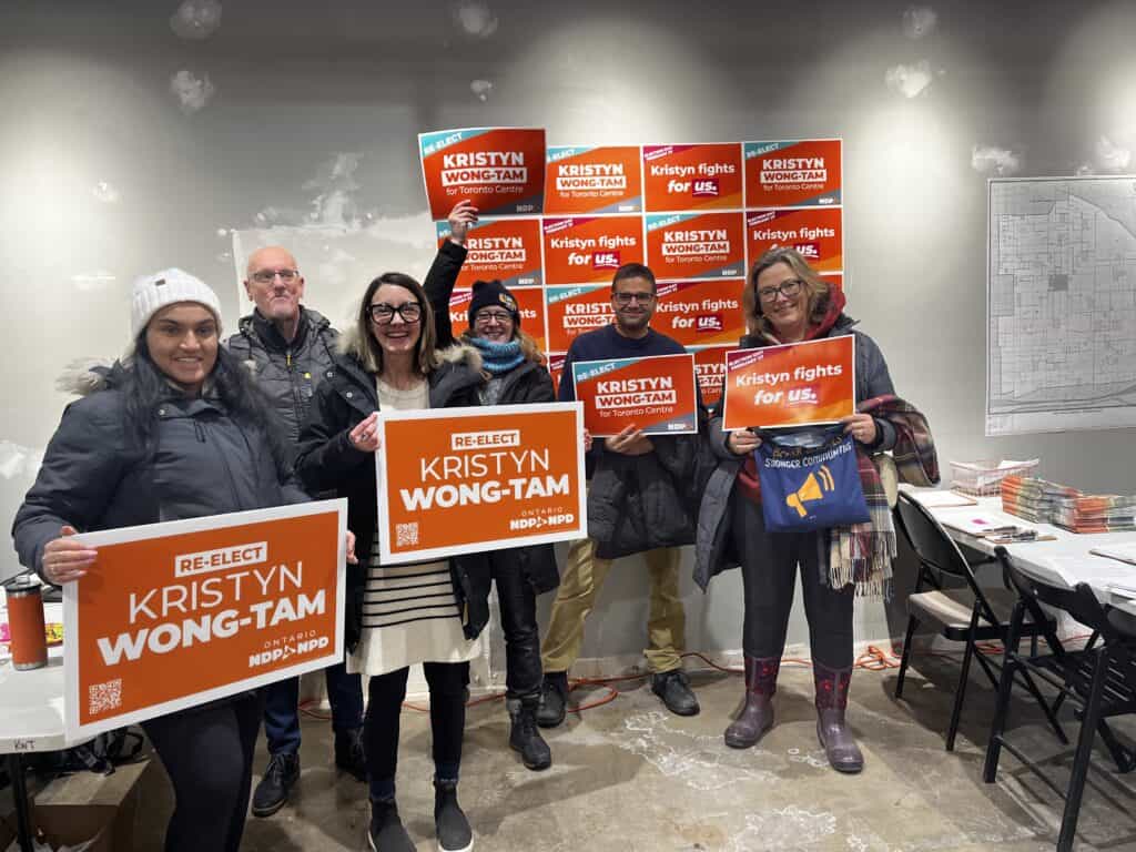 Un groupe de personnes dans un bureau de campagne tenant des affiches de campagne oranges.