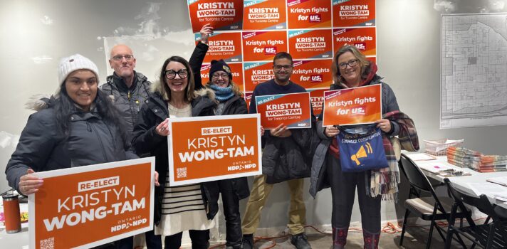 Un groupe de personnes dans un bureau de campagne tenant des affiches de campagne oranges.