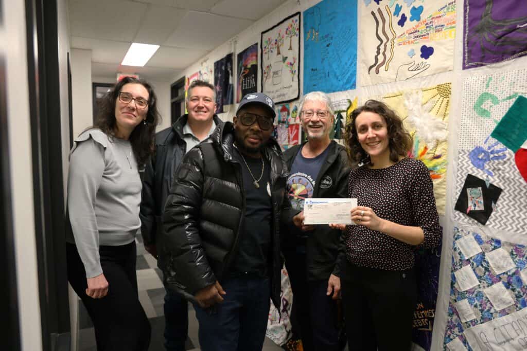 Five people taking a photo in an office. One person is holding a cheque.