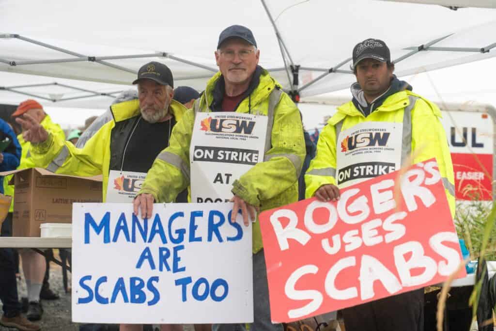 3 people holding signs that read managers are scabs too and Rogers uses scabs
